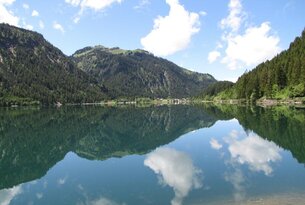 Bergsee mit Spiegelung von Bergen und Wolken im Wasser