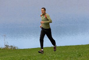 Mann joggt auf einer grünen Wiese vor blauem Hintergrund
