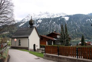 Kleine Kapelle vor Häusern und schneebedecktem Berg