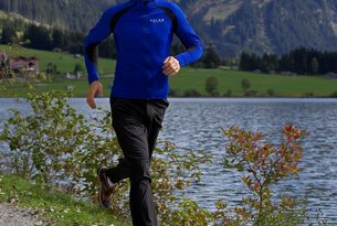 Mann in blauer Sportkleidung joggt an einem See vor Bergkulisse