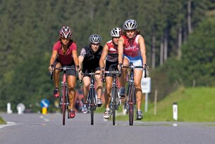 Vier Radfahrerinnen mit Helmen fahren auf einer Straße