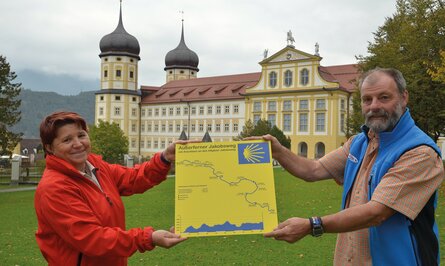 Zwei Personen halten gelbe Karte mit Wanderweg vor Schloss mit Türmen