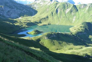 Bergsee eingebettet in grüne Hügel und Berge
