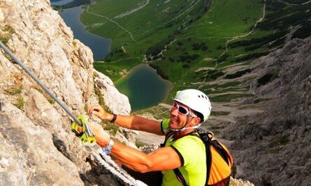 Kletterer am Felsgrat mit Seil, im Hintergrund Berglandschaft mit Seen