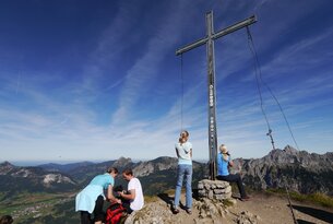 Menschengruppe am Gipfelkreuz mit Bergpanorama im Hintergrund