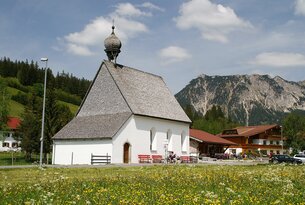 Kleine weiße Kirche auf grüner Wiese vor Bergkulisse