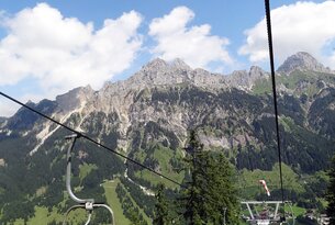 Sessellift vor Bergpanorama mit blauem Himmel und Wolken