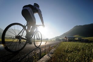 Radfahrer auf Landstraße vor Bergkulisse im Gegenlicht