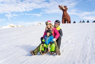 Familie fährt mit Schlitten im Schnee, Mammut im Hintergrund