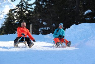 Mann und Frau sitzen auf Schlitten im Schnee
