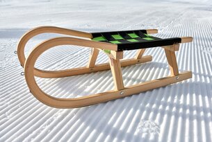 Holzschlitten mit grün-schwarzem Sitz auf Schnee