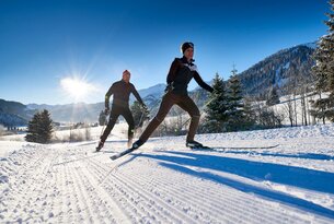 Zwei Personen beim Langlaufen in verschneiter Landschaft mit Bergen im Hintergrund