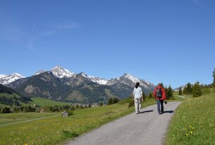 Wanderer auf Weg vor Bergpanorama mit schneebedeckten Gipfeln und blauem Himmel