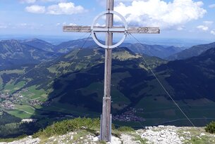 Gipfelkreuz auf Bergspitze vor Berglandschaft und blauem Himmel