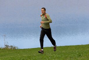 Mann joggt auf einer grünen Wiese vor blauem Himmel