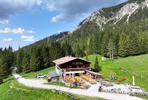Berghütte mit Biergarten vor bewaldetem Berg unter blauem Himmel