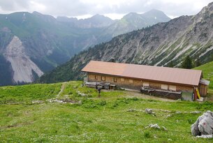 Hütte in den Bergen vor bewaldetem Hang und Gipfeln