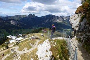 Frau steht auf Felsen, blickt auf Berglandschaft mit Häusern und Gleitschirmfliegern