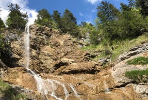 Wasserfall stürzt über Felsen, umgeben von Bäumen und blauem Himmel