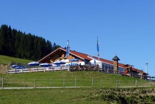 Berghütte mit rotem Dach auf grüner Wiese unter blauem Himmel