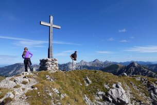 Gipfelkreuz auf Berg, zwei Wanderer, Bergpanorama im Hintergrund