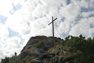 Gipfelkreuz auf felsigem Berg unter bewölktem Himmel