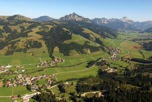 Grüne Hügellandschaft mit Dörfern vor Bergpanorama unter blauem Himmel