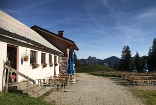 Hütte mit Tischen und Bänken vor Berglandschaft unter blauem Himmel