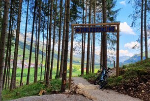 Sign Zirleseckline at the edge of the forest with mountain bike and view of the mountains