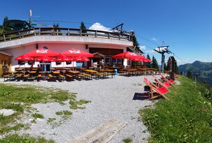 Bergrestaurant mit rotem Sonnenschirm und Liegestühlen auf Kiesfläche bei Sonnenschein