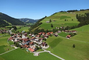 Dorf in grüner Hügellandschaft unter blauem Himmel
