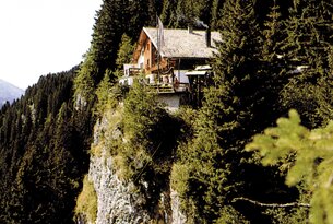 Holzhaus auf Felsklippe, umgeben von Bäumen