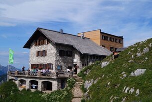 Berghütte aus Stein mit Terrasse und Holzanbau auf einem Hügel