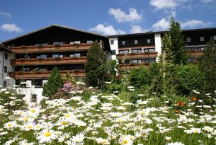 Hotel mit Balkonen hinter einer Wiese voller Gänseblümchen