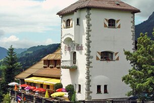 Weißes Gebäude mit Turm und Restaurant vor Berglandschaft