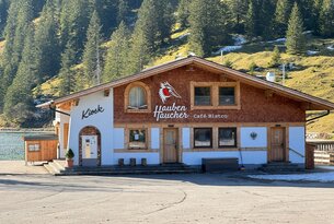 Holzhaus "Hauben Taucher Café Bistro" mit Kiosk vor bewaldetem Berghang