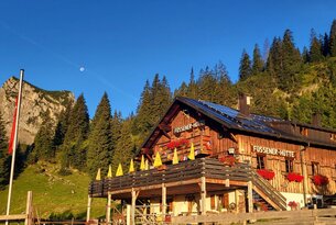 Hölzerne Berghütte mit Balkon vor bewaldetem Hang unter blauem Himmel