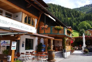 Pension Bergheim mit Holzfass und Tischen vor Bergkulisse