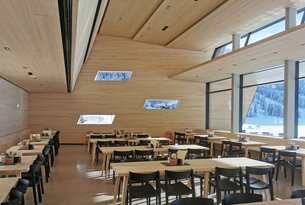 Helles Restaurant mit Holzwänden, Tischen und Stühlen, Blick durch Fenster auf verschneite Landschaft