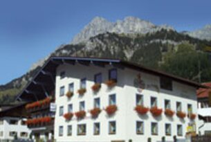 Weißes Gebäude mit roten Blumenkästen vor Bergkulisse