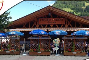 Café-Restaurant mit Holzfassade und blauen Sonnenschirmen vor Bergkulisse