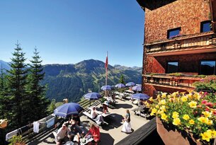 Terrasse eines Berghotels mit Gästen, Blick auf Berglandschaft