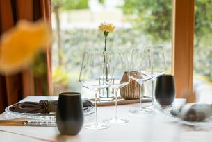 Gedeckter Tisch mit Weingläsern, Vase mit gelber Blume und Dekoration vor Fenster