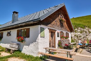 Hütte mit weißen Wänden, Holzschindeln und roten Blumenkästen vor blauem Himmel
