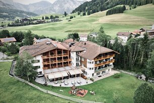 Hotel mit rotem Dach vor grüner Landschaft mit Bergen