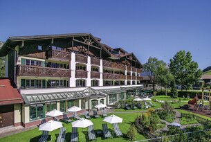Hotelgebäude mit Balkonen, Liegestühlen und Sonnenschirmen auf einer grünen Wiese