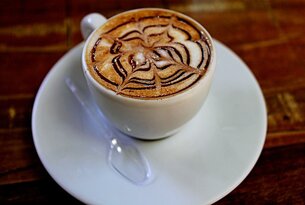 Cappuccino mit kunstvollem Muster aus Schokoladensirup in weißer Tasse auf Untertasse