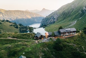 Berglandschaft mit See, Hütte und bewaldeten Hängen im hellen Tageslicht