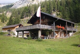 Holzhütte mit Balkon vor Berglandschaft und Wiese