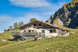 Hütte mit Holzfassade vor Berglandschaft unter blauem Himmel